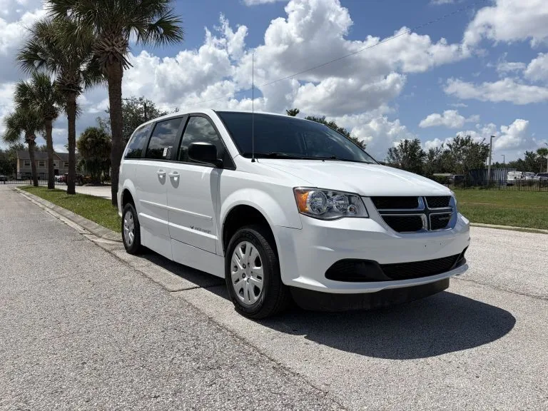 White wheelchair accessible Dodge Grand Caravan parked outdoors, seen from the front passenger side where the ramp deploys